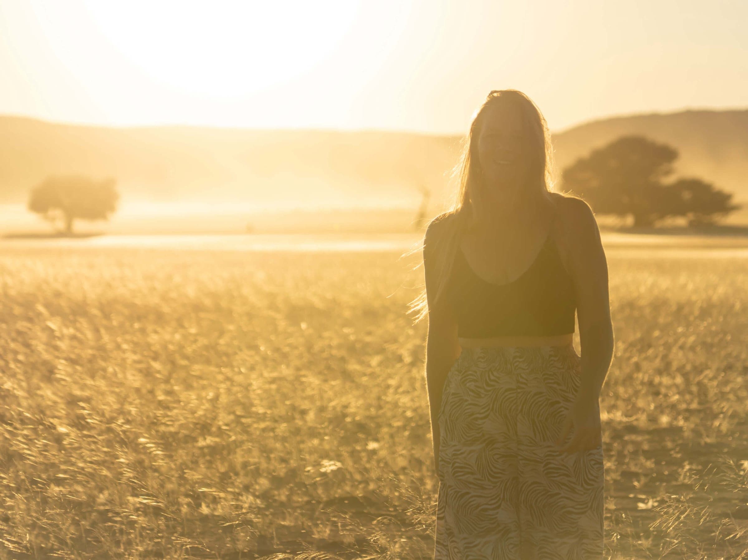 Léa de dos dans un champ d'herbes hautes, à contre-jour au soleil couchant