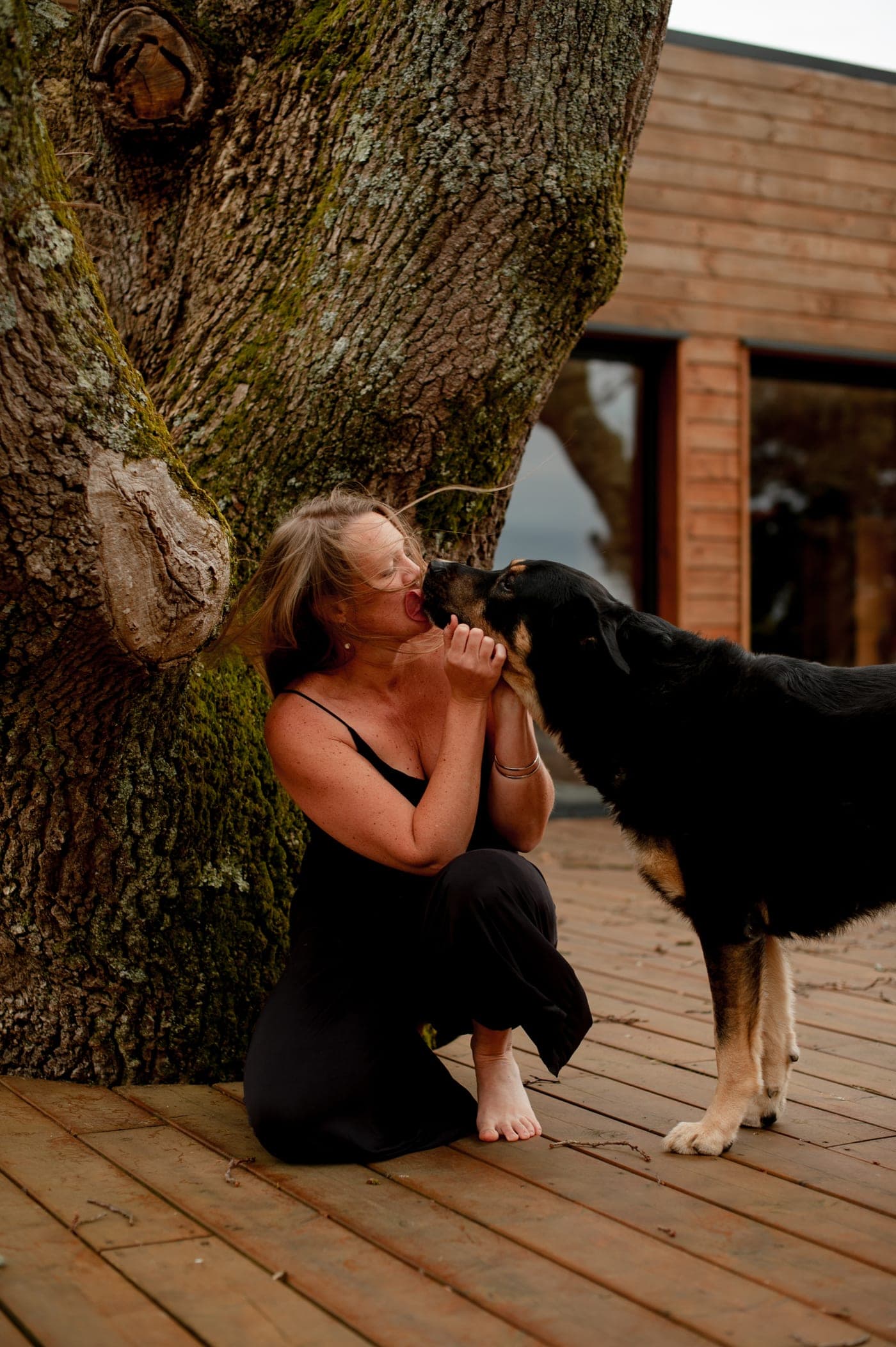 Léa accroupie contre un arbre, en échange avec un chien noir