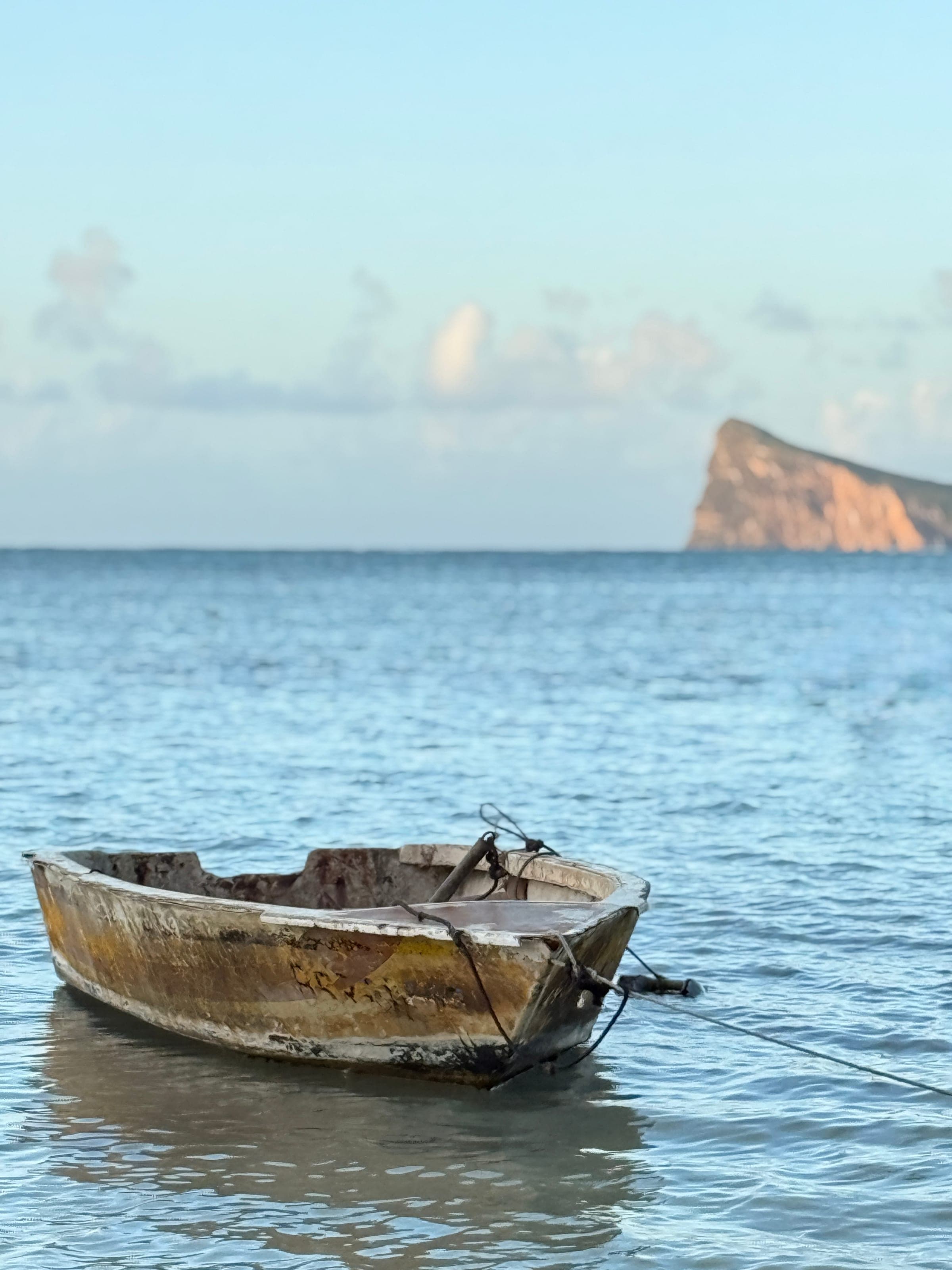 Une barque amarrée dans l'eau turquoise, l'îlot du Coin de Mire à l'horizon