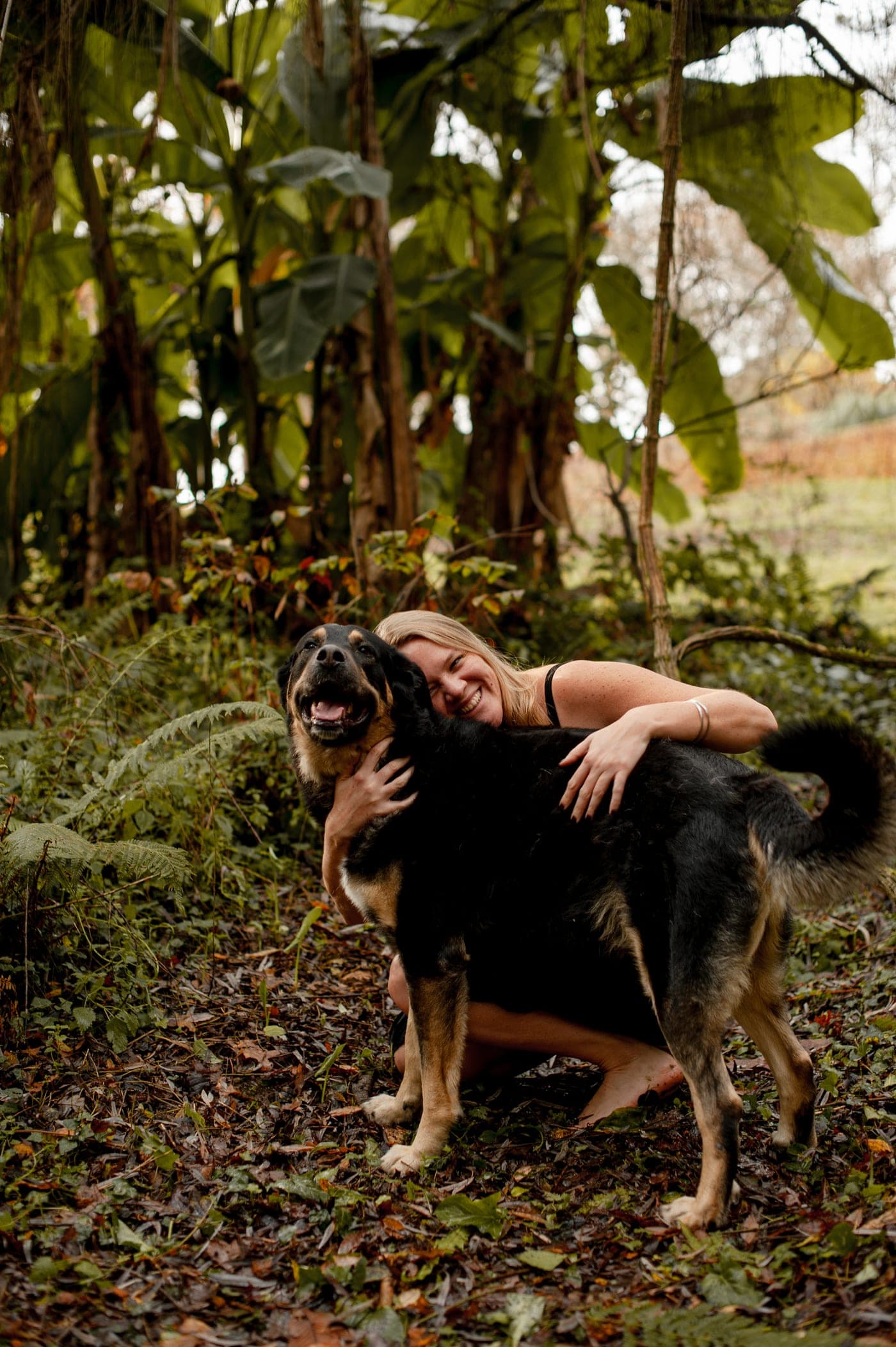 Léa en forêt, penchée vers un chien noir qui la regarde